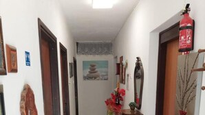 Ein Flur mit Fliesenboden, einer Tür mit rotem Feuerlöscher, einem gerahmten Bild an der Wand und einem kleinen Tisch mit Blumen.