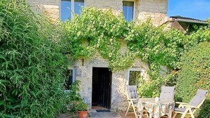 Ein Steinhaus mit einer gepflasterten Terrasse, einer Tür und einem Tisch mit Stühlen.