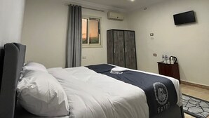 A modern hotel room with a bed, a wardrobe, a flat-screen TV, and a window with curtains. - Panorama 3 Pyramids View Inn (Giza)