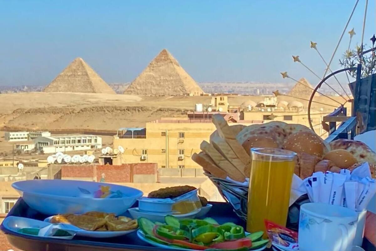 A table with food and drinks, a view of the pyramids, and buildings in the background.