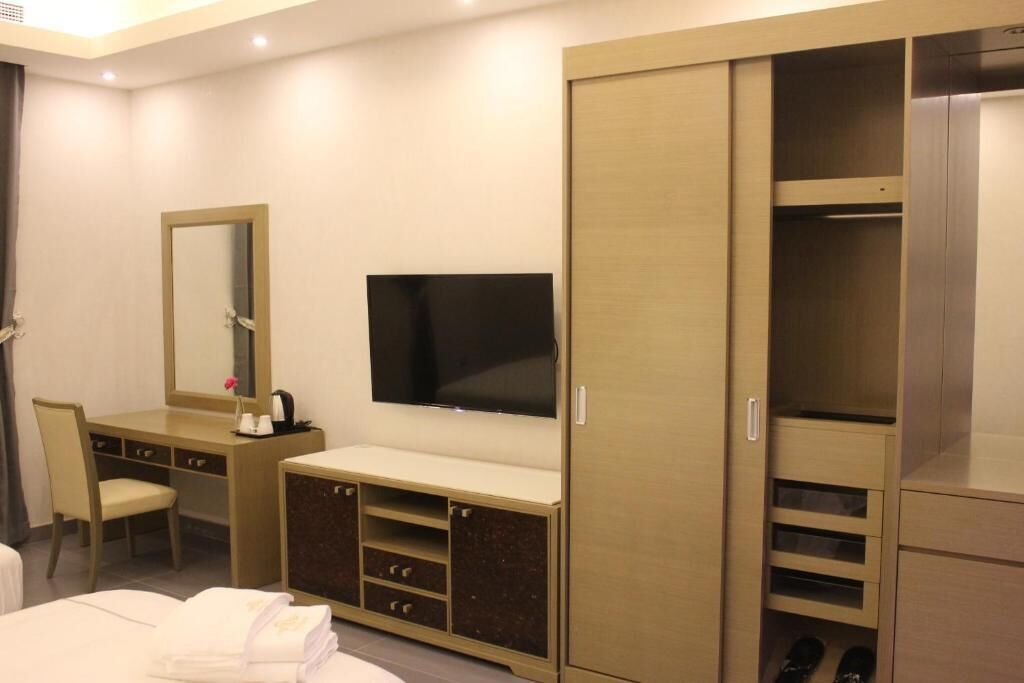 Habitación de hotel con cama, escritorio con silla, televisión y armario con zapatero.