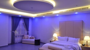 Un dormitorio moderno con una cama grande, mesitas de noche, un banco y una ventana con cortinas.