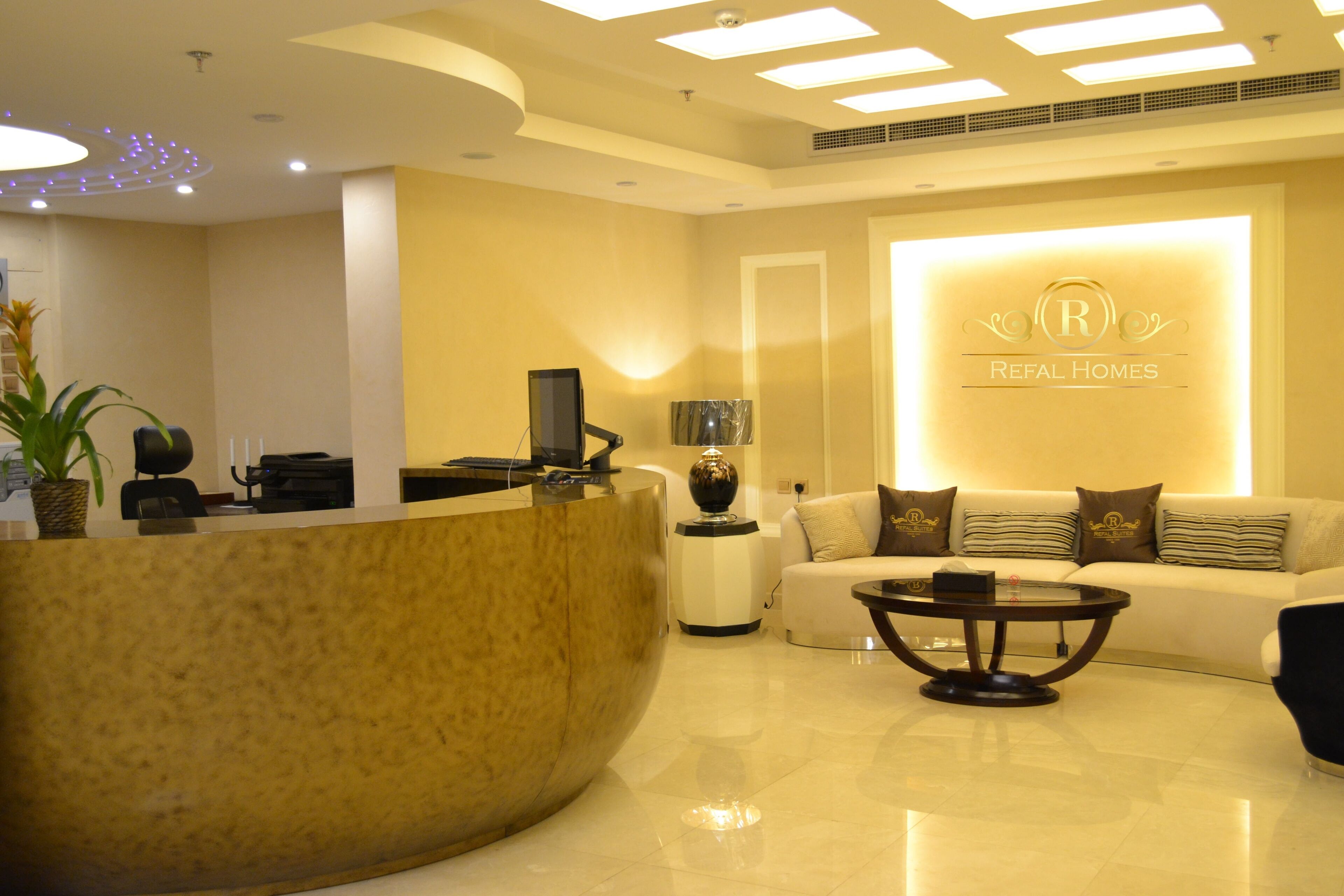 A reception area with a curved reception desk, a sofa, a coffee table, and a wall with a logo.