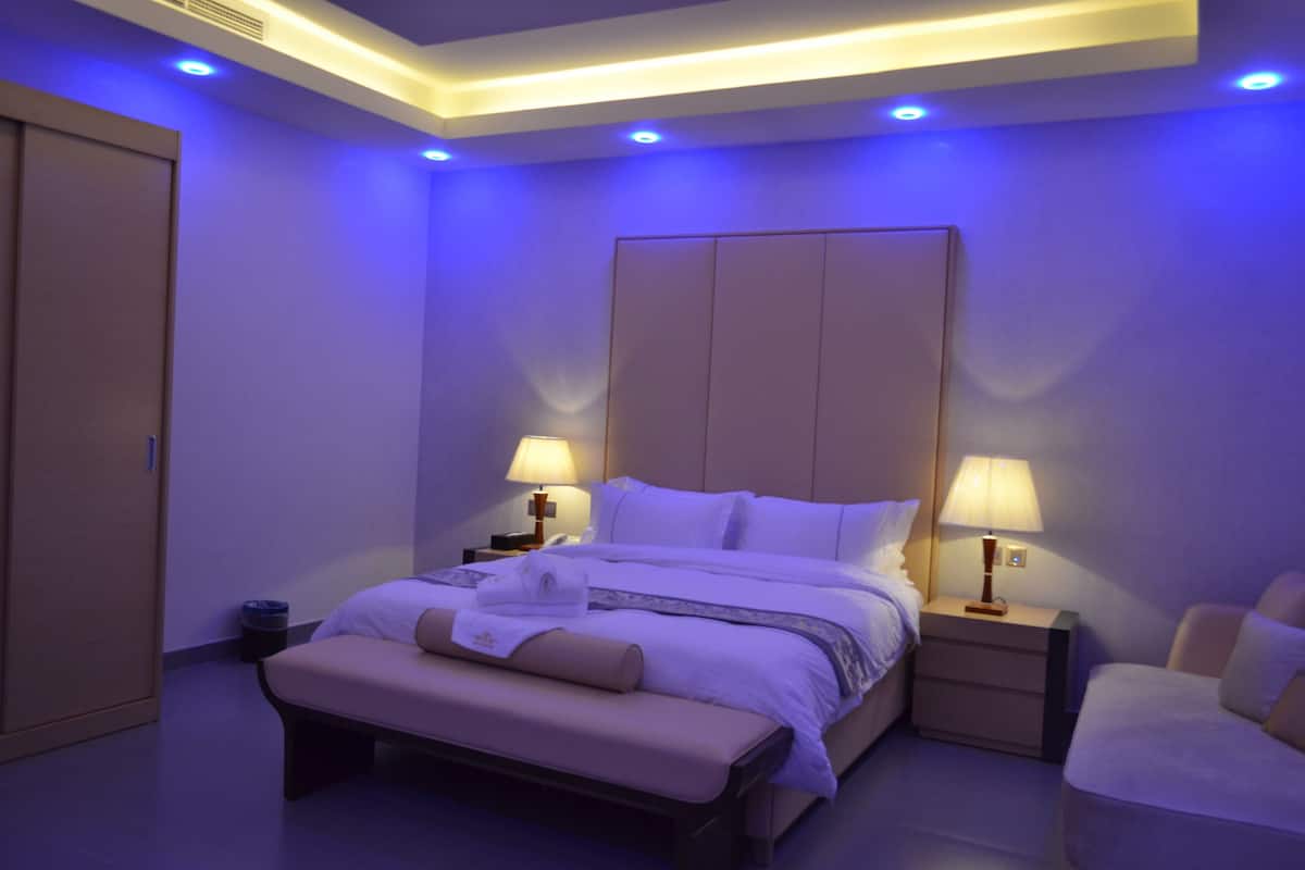 Une chambre d’hôtel avec un grand lit, des tables de chevet avec des lampes, un banc et une armoire.