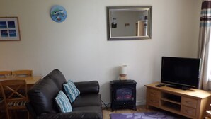 A living room with a black leather sofa, a small wooden table, a television, and a fireplace.