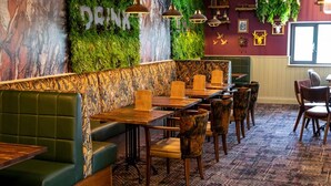 A restaurant with a green booth seating area, wooden tables, and chairs.