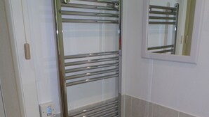 A bathroom with a chrome towel rack, a mirror, and a trash bin.