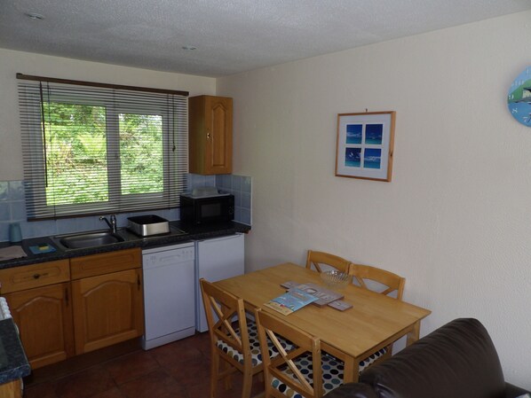 A compact kitchen with a sink, microwave, and dishwasher, a dining table with chairs, and a window with blinds.