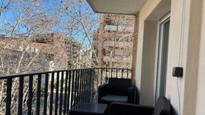 A balcony with two black wicker chairs and a small table, overlooking a tree and buildings. - Aparta 4 Habitaciones Terrassa Centro, Parking (Terrassa)