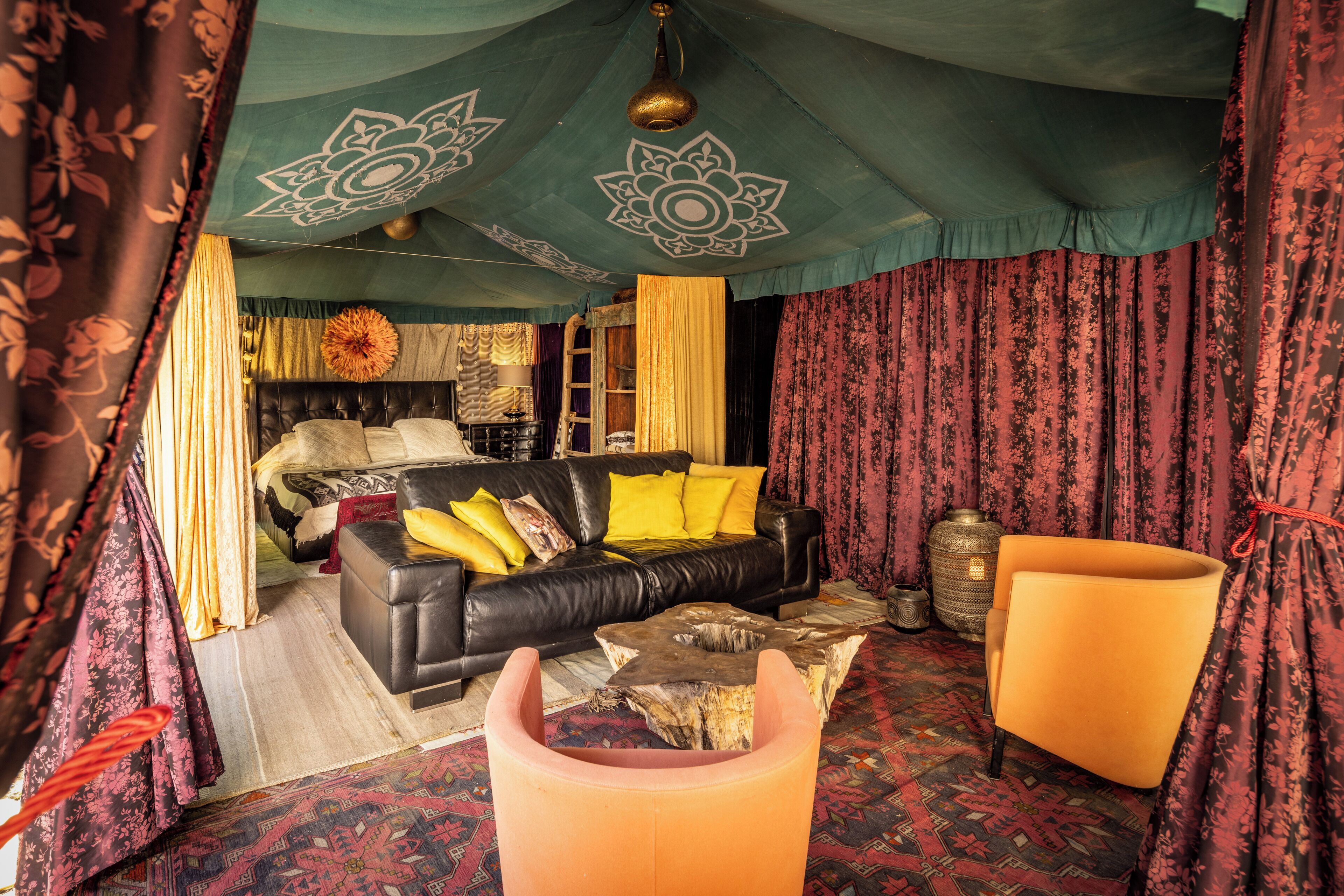 A room with a black leather sofa, yellow cushions, a wooden coffee table, and a bright orange armchair.