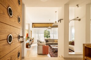 Un salon moderne avec un canapé, une table basse et des coussins décoratifs. On peut voir, à gauche, un meuble en bois doté de poignées rondes.