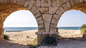 Een oude stenen boogpoort die leidt naar een zandstrand, met de zee op de achtergrond.