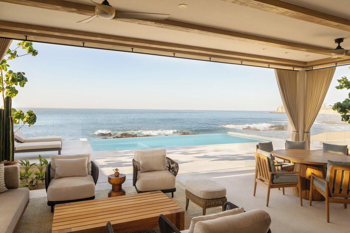 A beachfront patio with a pool, seating, and a view of the ocean.