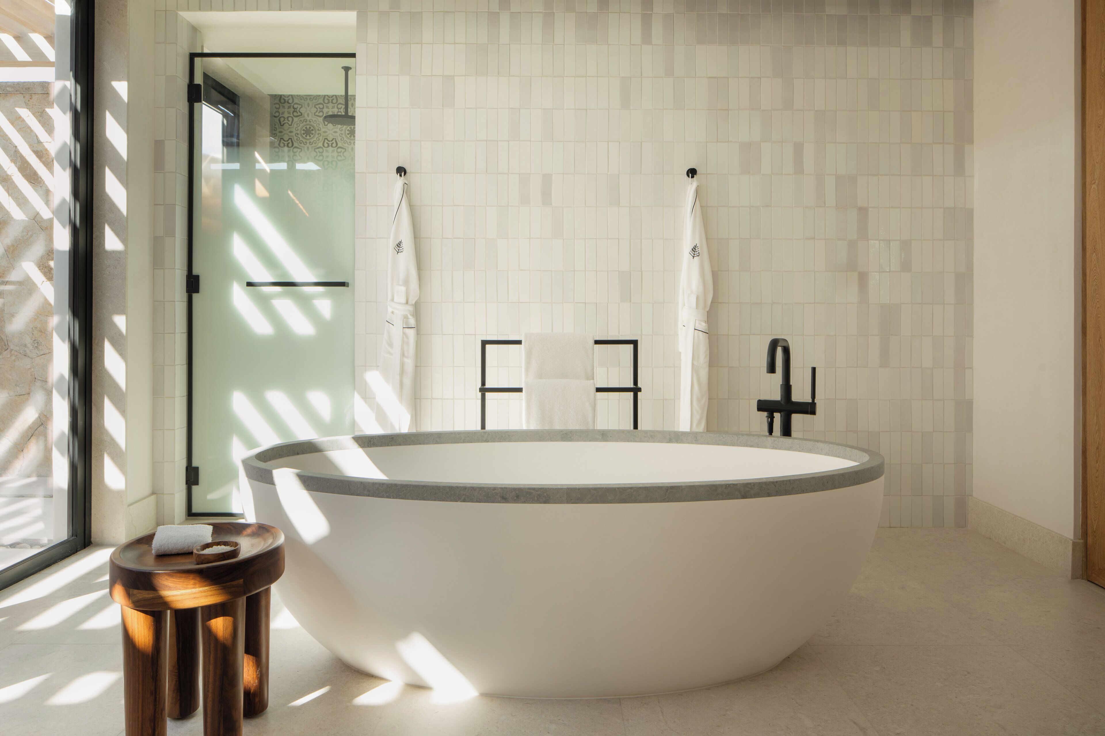 Une salle de bain moderne avec une baignoire sur pieds, une douche en verre et un petit tabouret en bois sur lequel est posée une serviette.