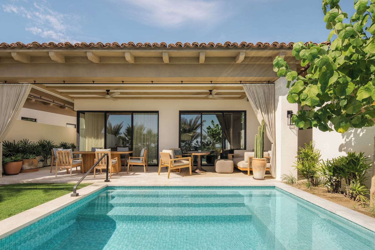 A swimming pool with a covered patio area, outdoor furniture, and potted plants.