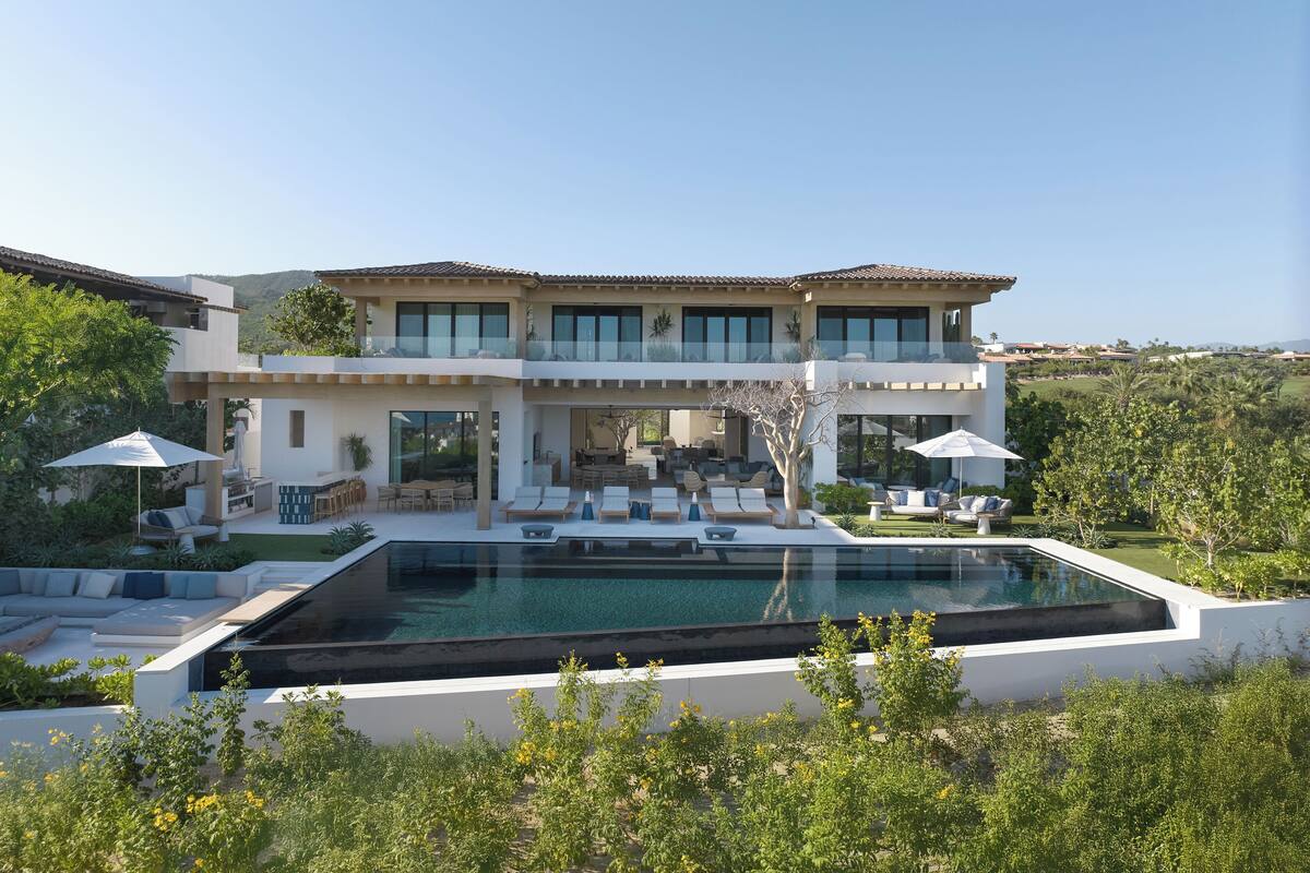 A modern two-story house with a large swimming pool, outdoor seating, and a scenic view.