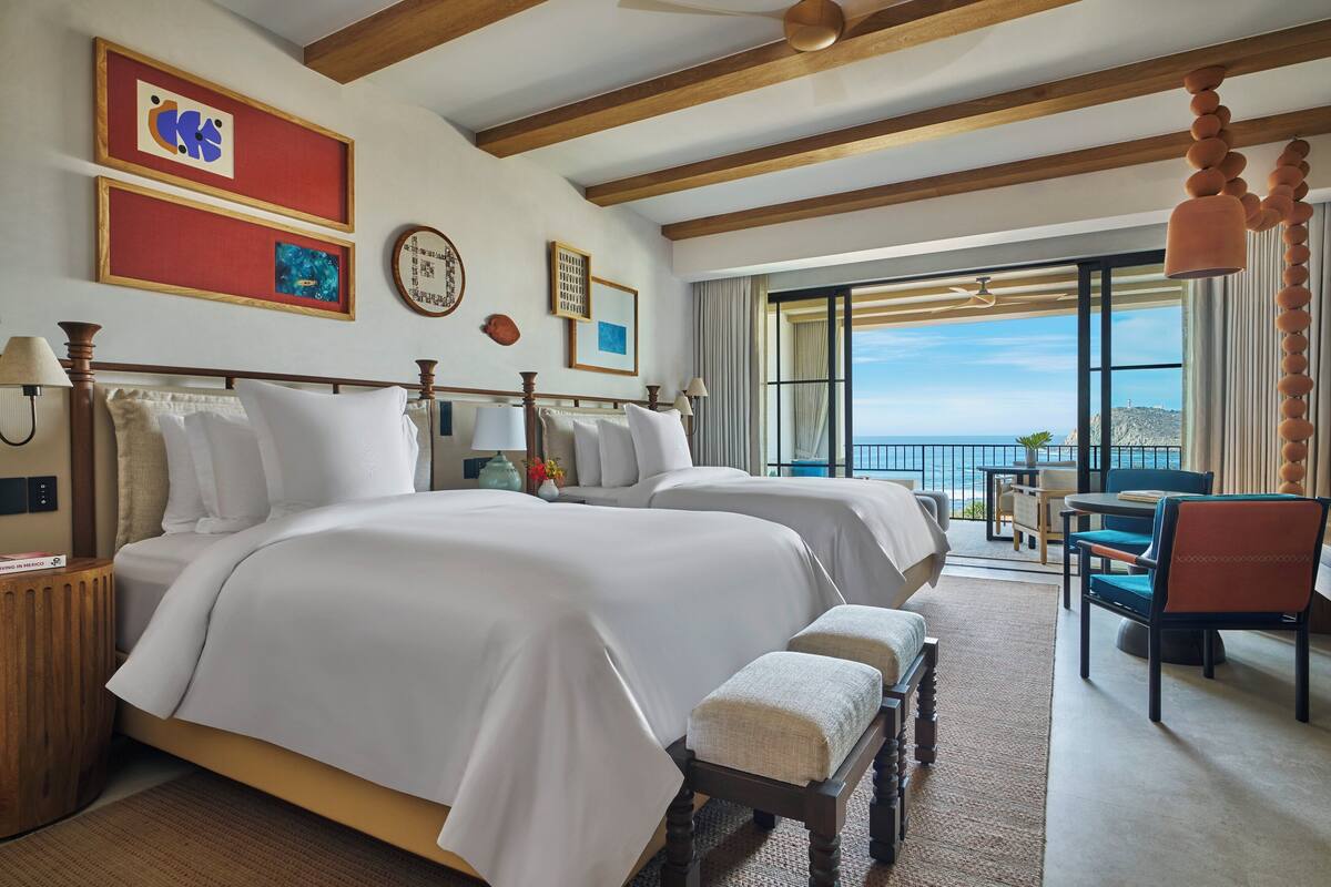 A hotel room with two beds, a balcony with a view, and a dining area.