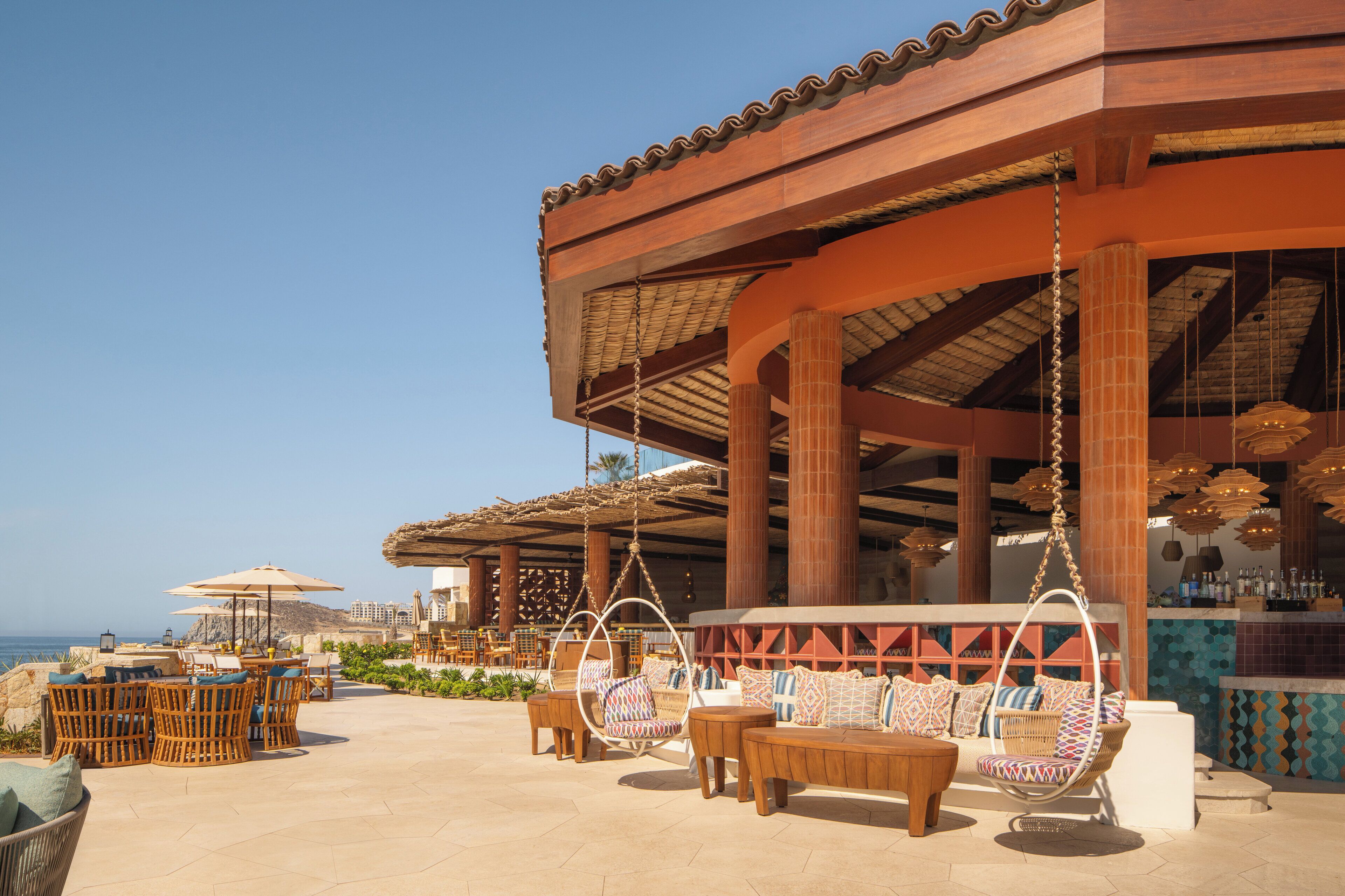Un espace extérieur aménagé avec des meubles en osier et un fauteuil suspendu, offrant une vue sur la plage.