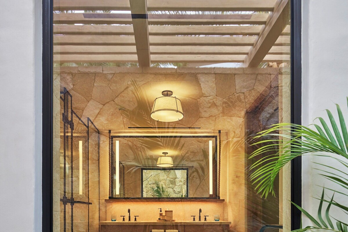 A modern bathroom with a stone wall, a large mirror, a round table, and a ceiling light.