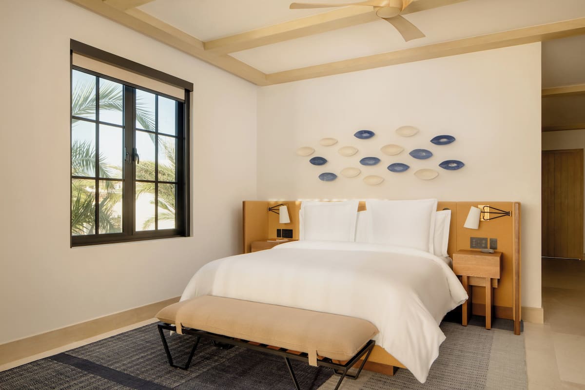 A bedroom with a bed, a bench, a nightstand, a wall-mounted lamp, and a ceiling fan.
