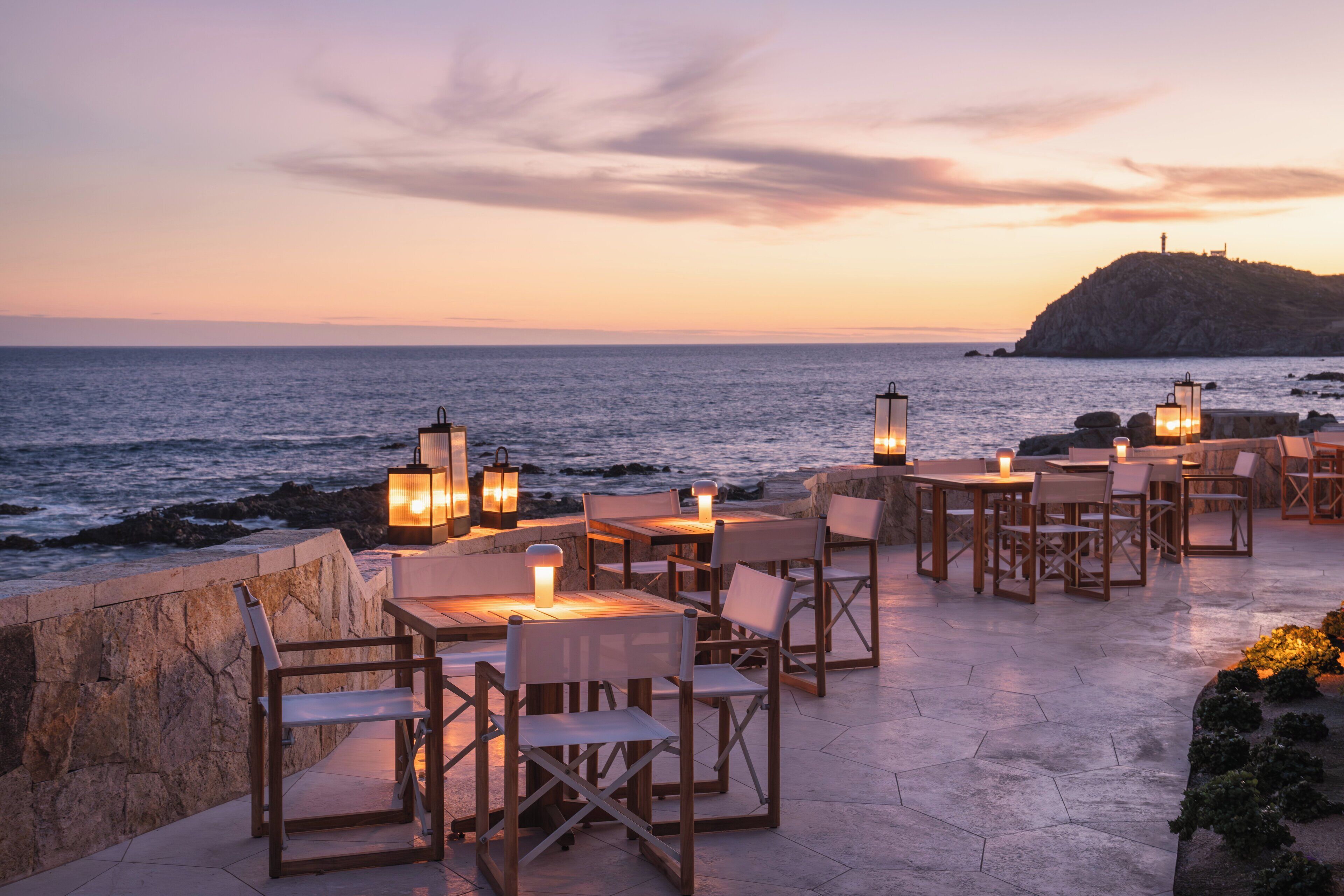 Un espace extérieur aménagé avec des tables et des chaises, offrant une vue sur la mer au coucher du soleil.