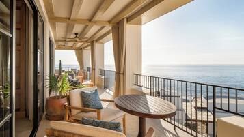 A balcony with a view of the ocean, furnished with wicker chairs, a round table, and potted plants.