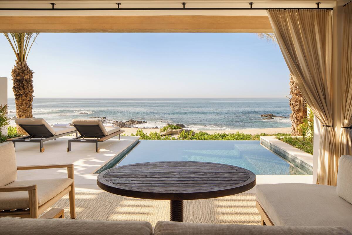 A poolside area with lounge chairs and a table, overlooking a beach and ocean.