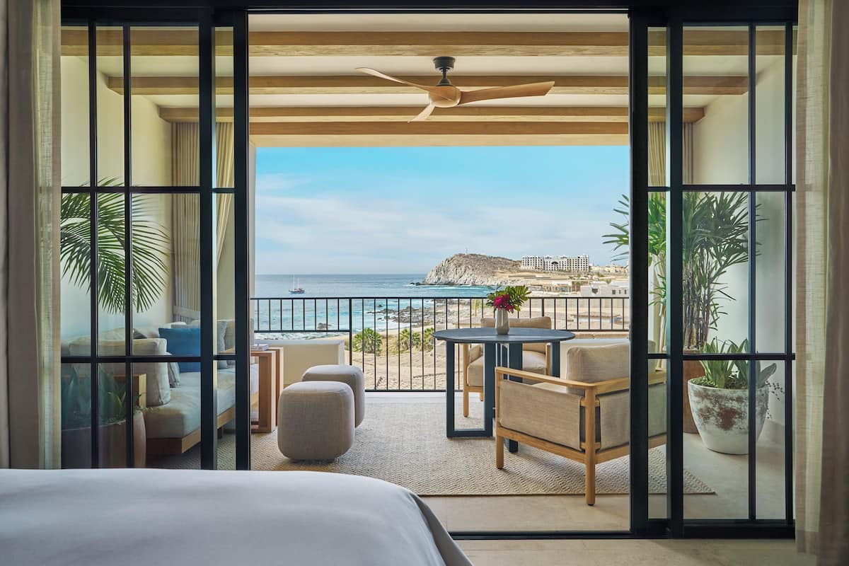 A balcony with a view of the sea, a bed, and a table with chairs.