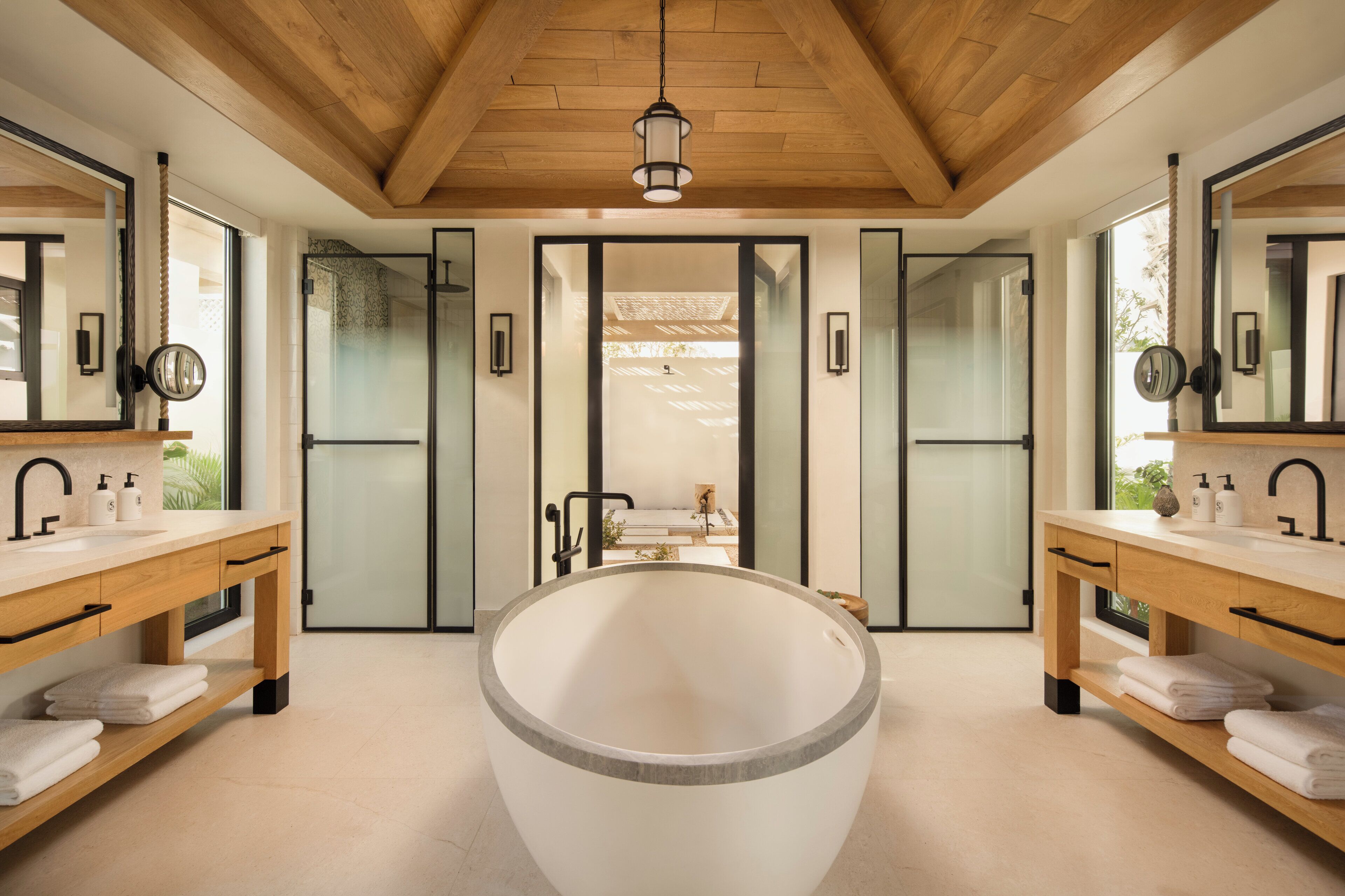 Een moderne badkamer met een vrijstaand ligbad, een houten wastafelmeubel met spiegel en uitzicht op het buitengebied door matglazen deuren.