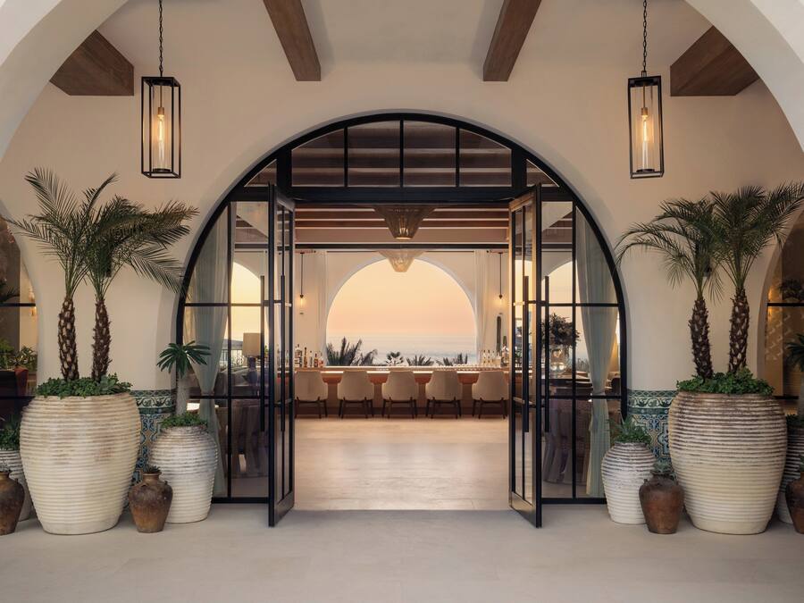 Una entrada arqueada con plantas en macetas grandes, una zona de bar con sillas y vistas al atardecer.