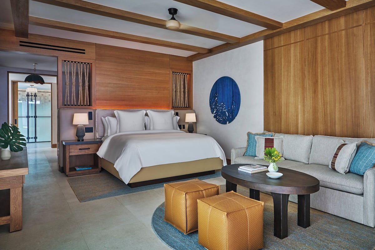 A modern hotel room with a large bed, a sofa, a coffee table, and a desk.