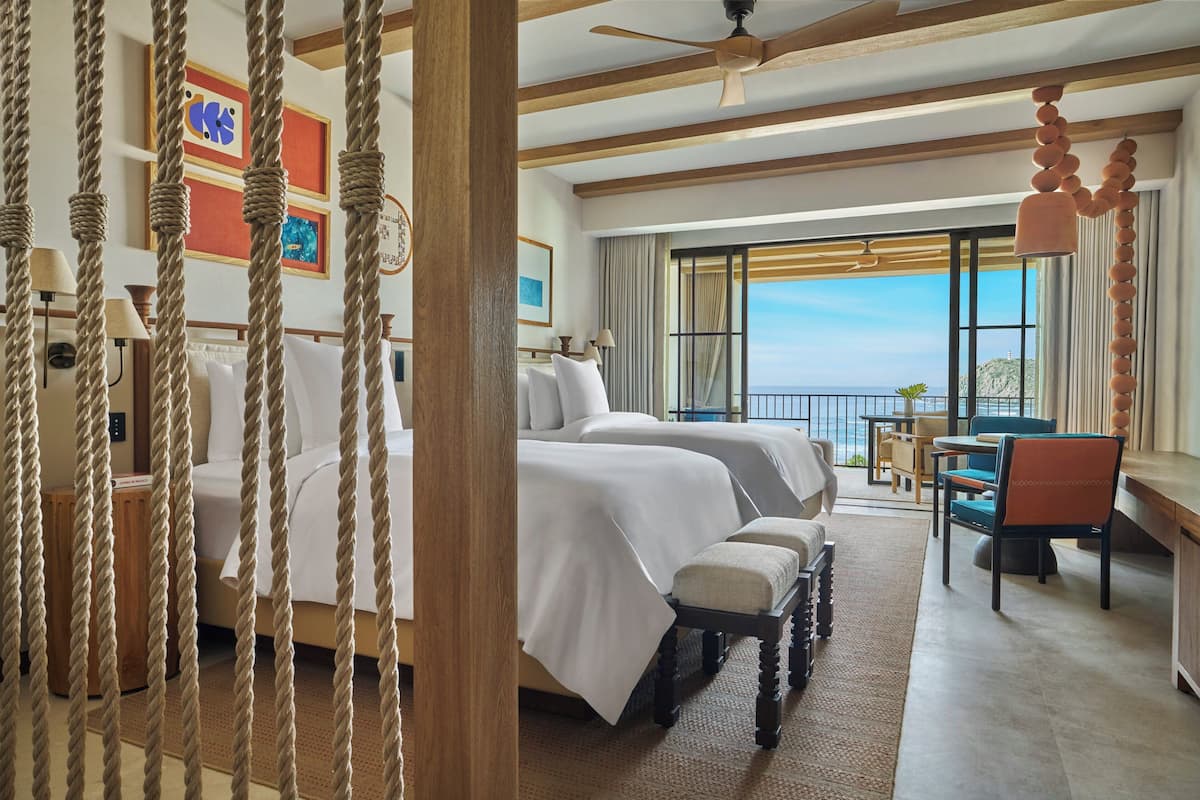 A hotel room with two beds, a desk, and a balcony with a view.