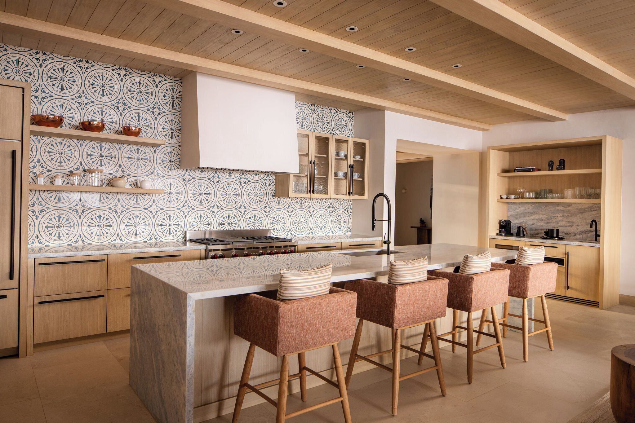 Une cuisine moderne dotée d’un îlot central, de tabourets de bar, de meubles en bois et d’un revêtement mural décoratif.