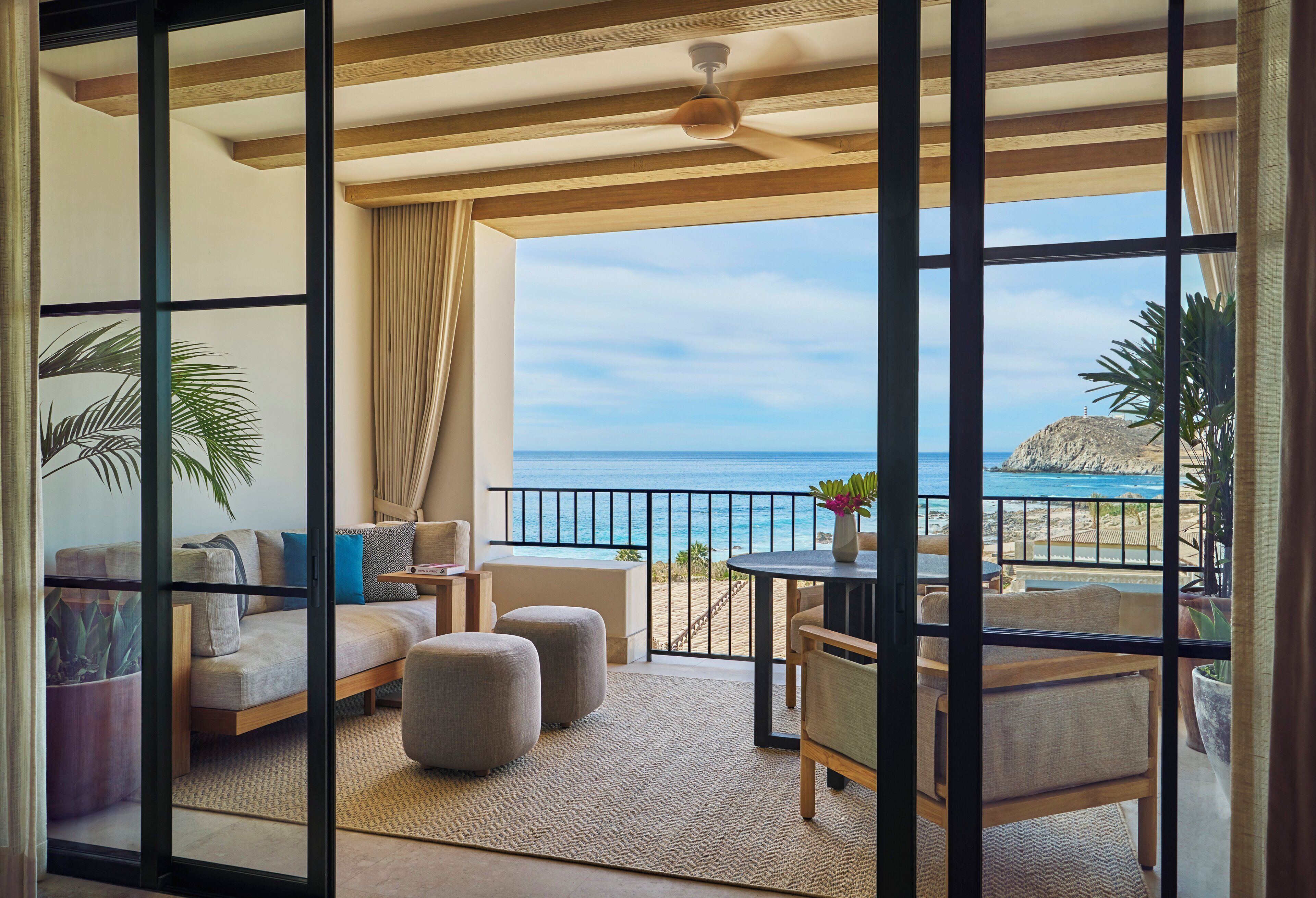 A balcony with a view of the sea, a sofa, ottomans, and a table with chairs.
