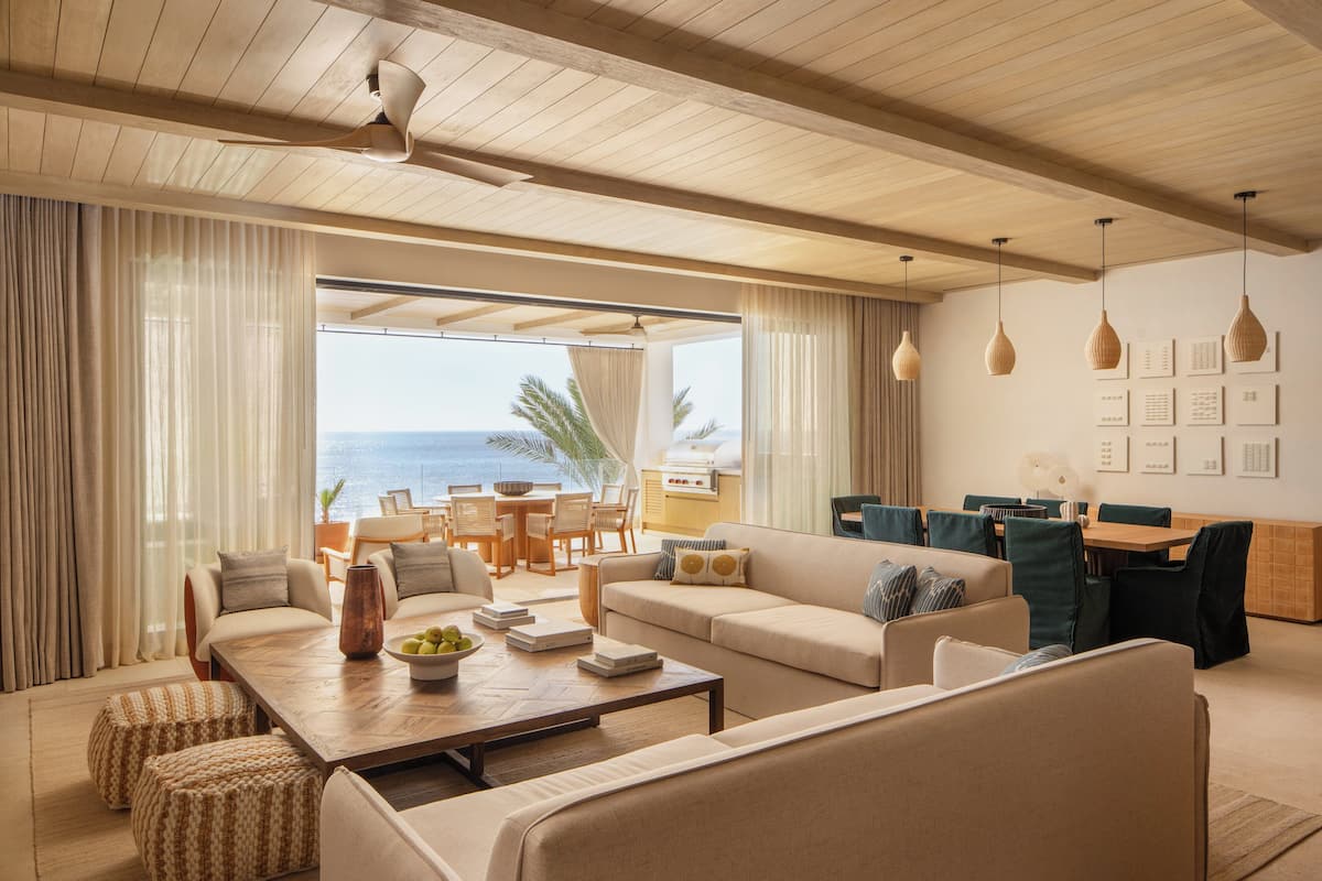 A spacious living area with a large window overlooking the ocean, a wooden ceiling, and a dining area with a view.