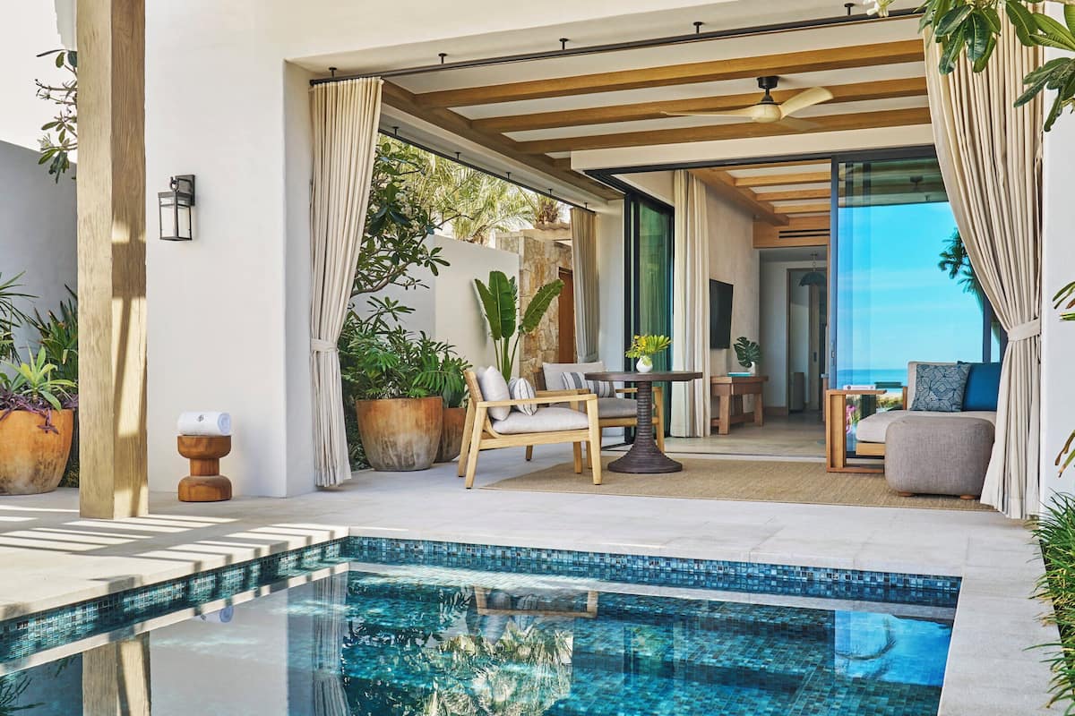 A modern outdoor pool area with a clear pool, wooden pergola, and seating under the shade.
