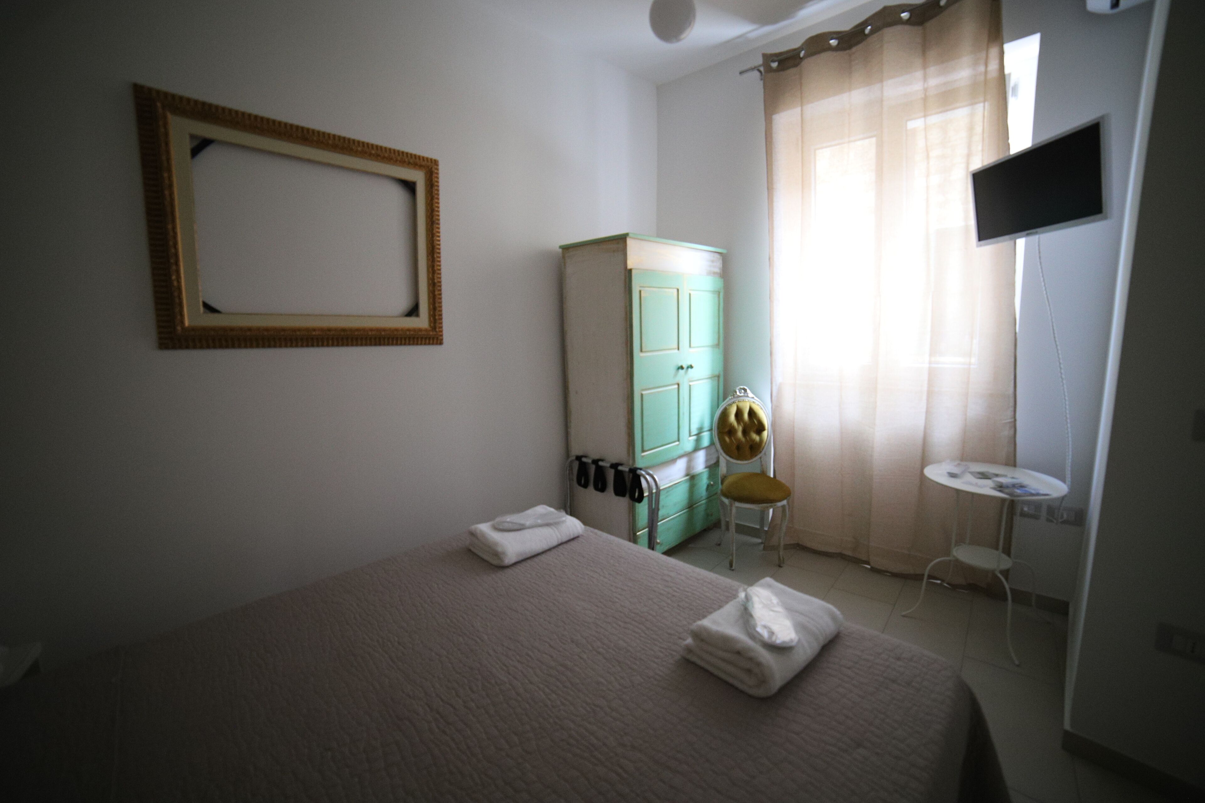 A hotel room with a bed, a green wardrobe, a small table, a chair, and a TV mounted on the wall.