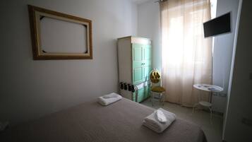 A hotel room with a bed, a green wardrobe, a small table, a chair, and a TV mounted on the wall.