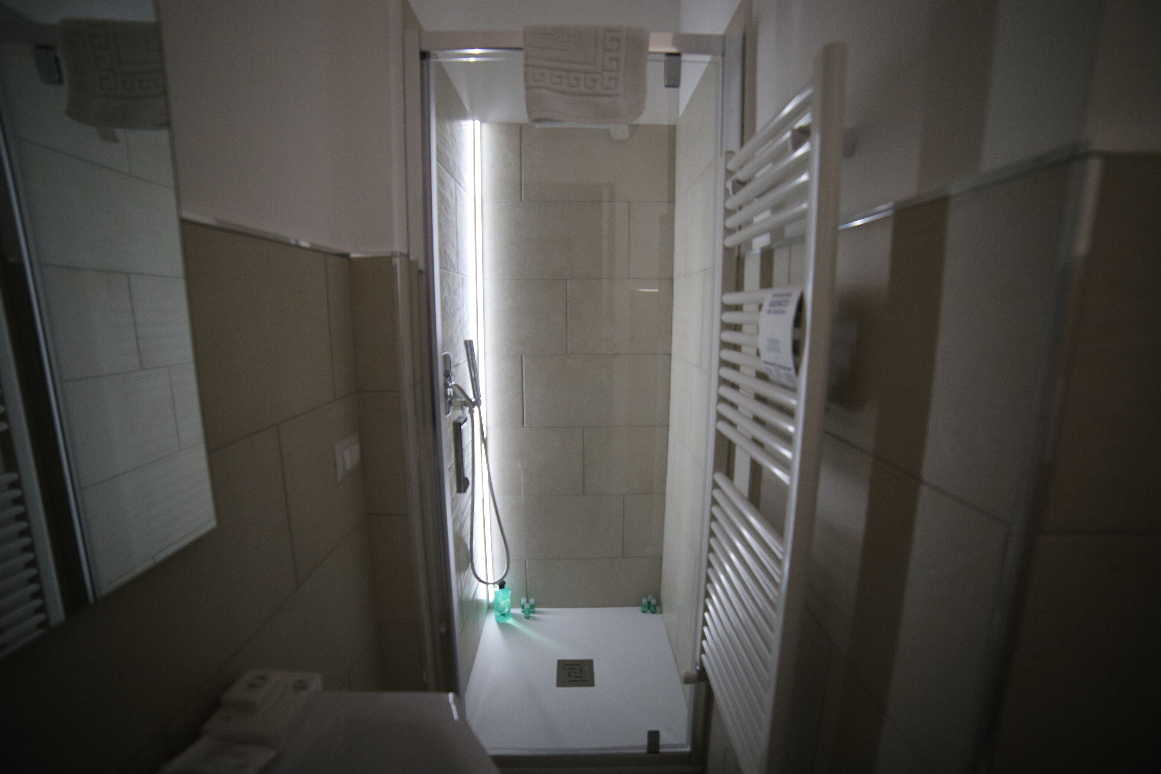 A narrow bathroom with a shower, tiled walls, and a towel rack.