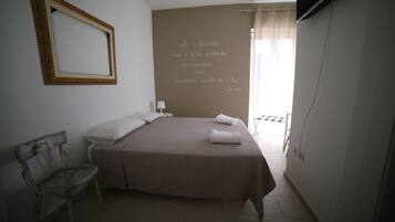 A bedroom with a bed, a chair, a mirror, and a wall with a quote.