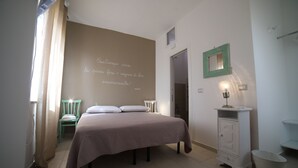 Quarto com cama, cadeira, penteadeira com espelho e parede com uma frase.