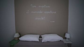 Un dormitorio con una cama, dos almohadas blancas, una mesita de noche verde y una pared con una cita motivacional en italiano.