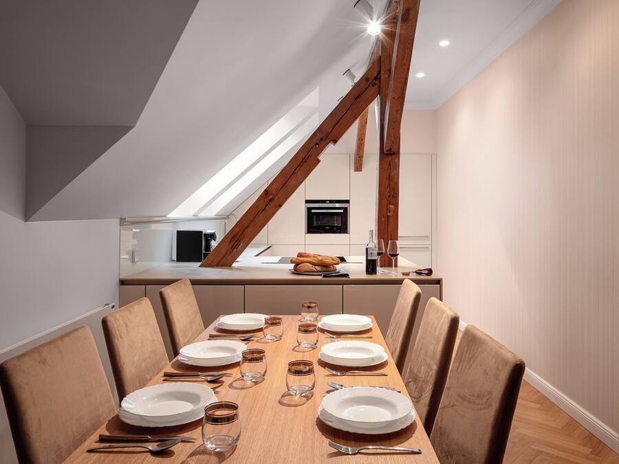 Een eetgedeelte met een houten tafel voor zes personen, een keuken op de achtergrond en een schuin dak.
