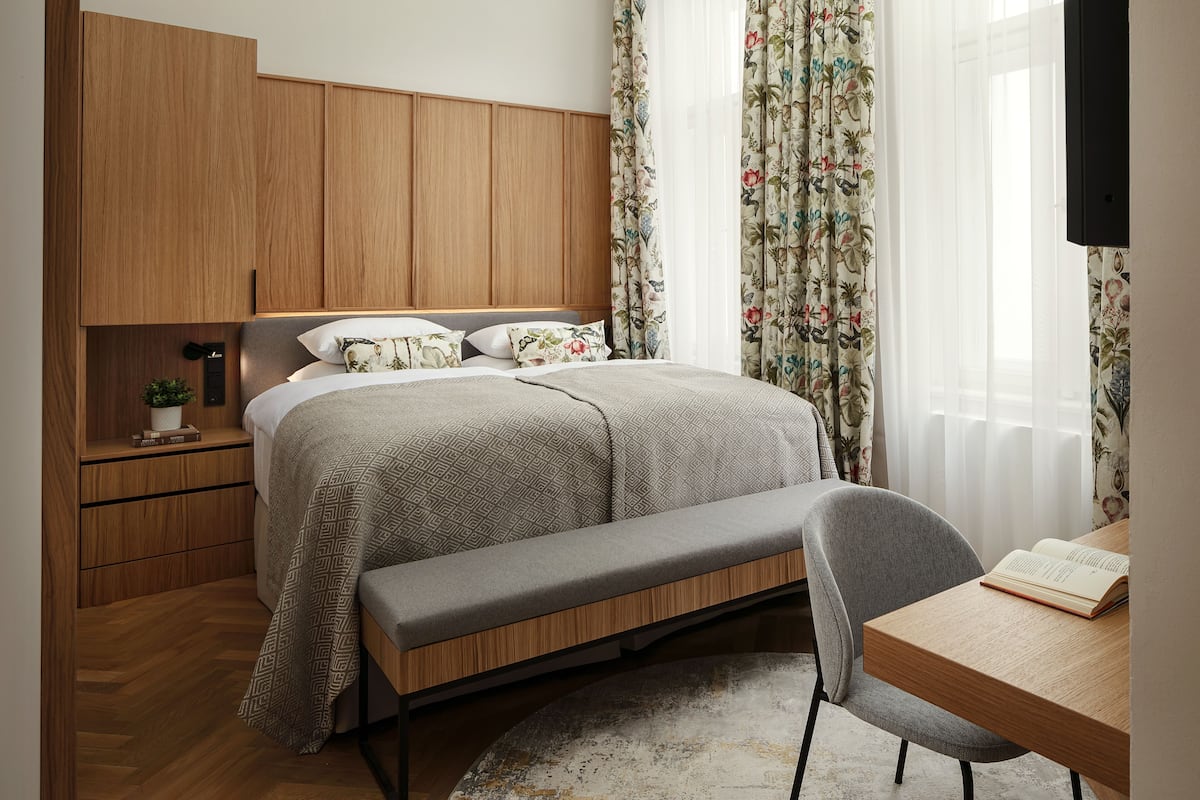 Un dormitorio con cama, banca, escritorio y cortinas.