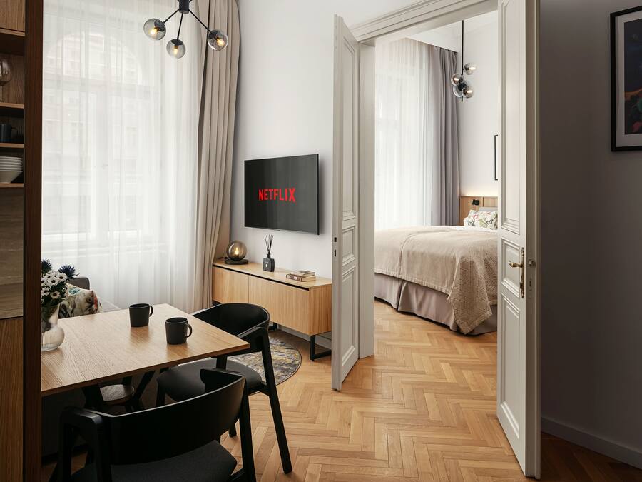 A modern hotel room with a dining area, a TV, and a bed.
