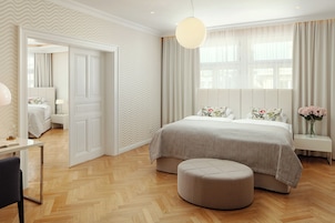 Quarto moderno com uma cama grande, mesa de cabeceira, uma cadeira e janela com cortinas.