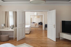 Ruime hotelkamer met houten vloer, groot bed, bureau met spiegel en televisie.
