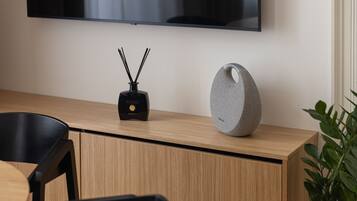 A modern room with a wooden desk, a flat-screen TV mounted on the wall, a black speaker, and a round grey speaker on the desk.