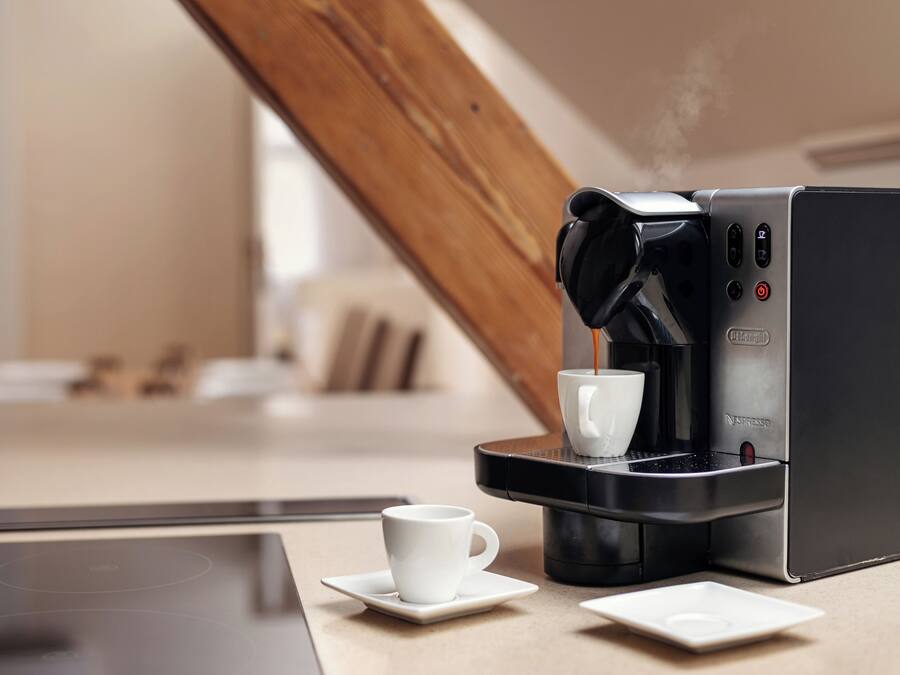 Una cafetera moderna con una taza de café sobre una mesa.