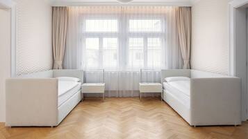 Quarto de hotel moderno com uma janela grande, dois sofás brancos, uma mesa pequena e um chão de madeira em padrão herringbone.